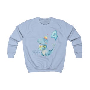 Puede incluir: Sudadera azul claro con una ilustraci&oacute;n de acuarela de un dinosaurio azul con un gorro de fiesta y un regalo. Un globo con el n&uacute;mero 4 flota cerca. El nombre "Matteo" est&aacute; escrito en cursiva debajo del dinosaurio.