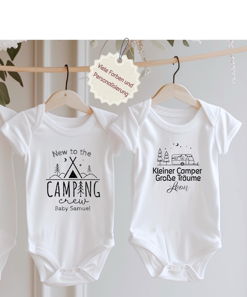 Könnte beinhalten: Zwei weiße Baby-Bodys hängen an Holzbügeln. Einer zeigt ein Camping-Design mit dem Text "New to the CAMPING crew Baby Samuel". Der andere hat ein Wohnmobil-Design mit deutschem Text.