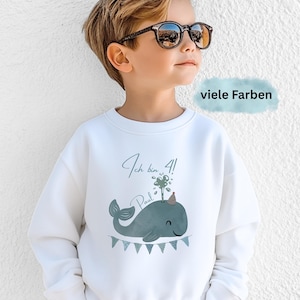 May include: White sweatshirt with a whale graphic, a party hat, and the text "Ich bin 4!" and "Paul". The whale is blue-green with a banner of small flags below. The text "viele Farben" is in a blue rectangle.