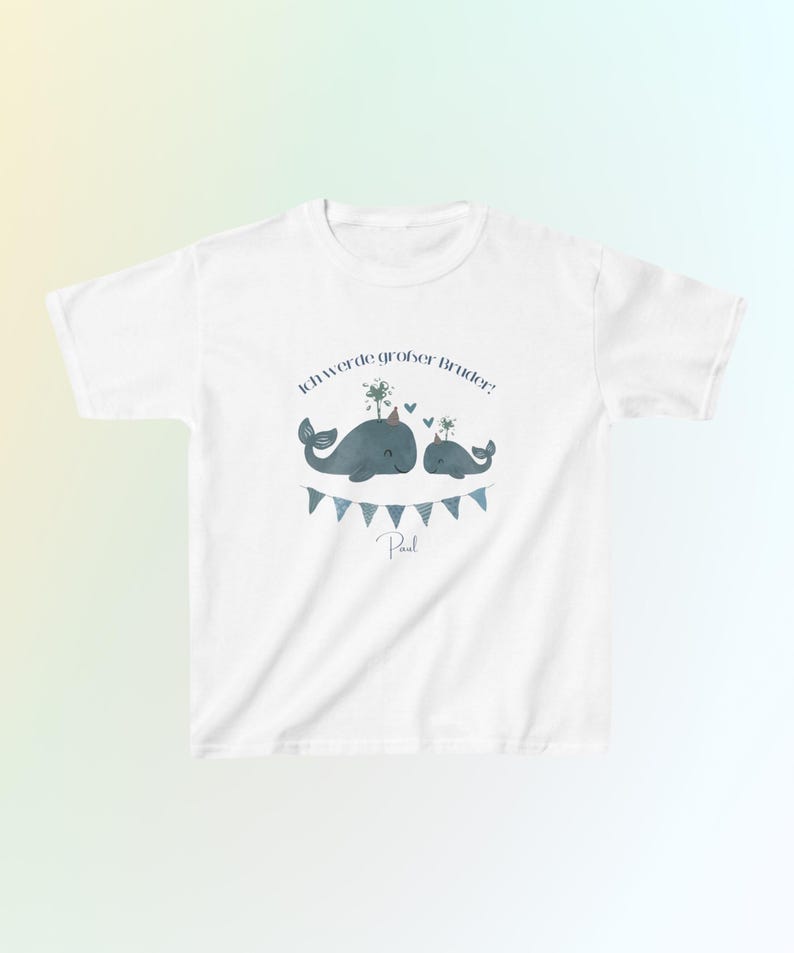 May include: A white short-sleeved t-shirt featuring a graphic of two blue whales, one larger than the other, wearing party hats. Above the whales is the text 'Ich werde gro&szlig;er Bruder!' and below them is a blue bunting banner with the name 'Paul'.