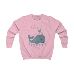May include: A light pink sweatshirt featuring a blue whale illustration with a party hat and a banner. The text "Ich bin 1!" and a name are above the whale. The sweatshirt has long sleeves and a crew neck.