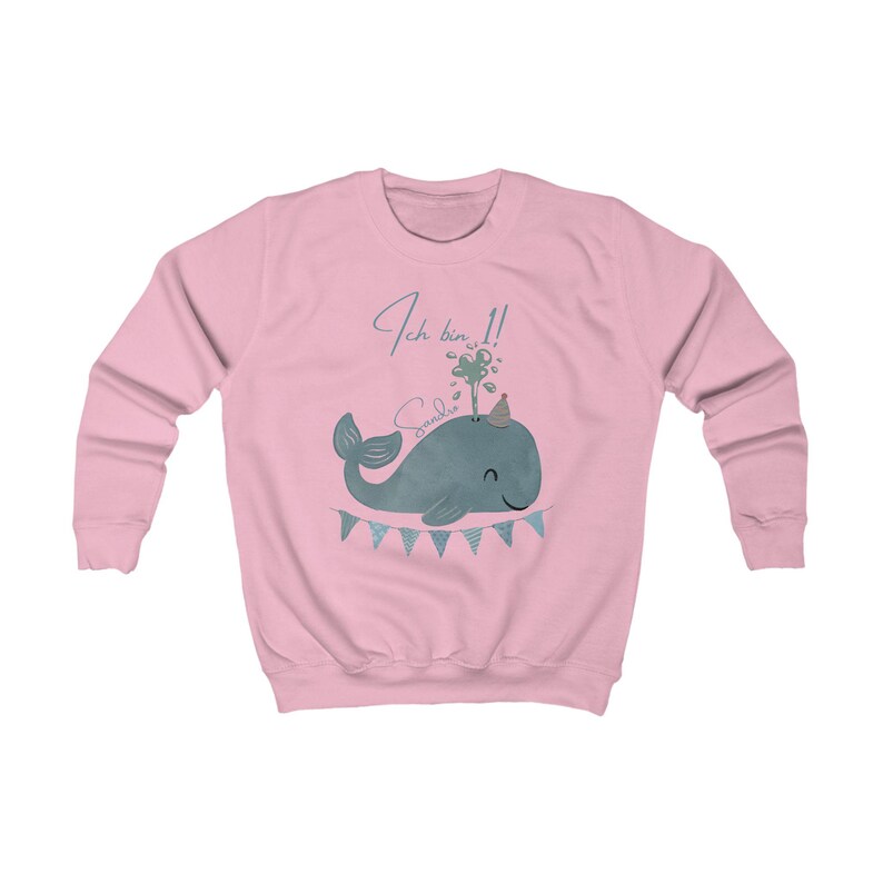 May include: A light pink sweatshirt featuring a blue whale illustration with a party hat and a banner. The text "Ich bin 1!" and a name are above the whale. The sweatshirt has long sleeves and a crew neck.