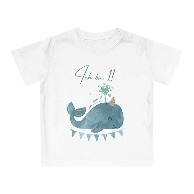 May include: White baby t-shirt with a blue watercolor illustration of a whale wearing a party hat and spouting water. The text "Ich bin 1! Levi" is written above the whale in blue script. A banner of blue pennants is below the whale.