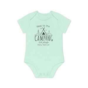 May include: A light green baby onesie with short sleeves. The front features the text "New to the CAMPING crew" with a tent and tree graphic. Below the text is "Baby Samuel" in a script font.