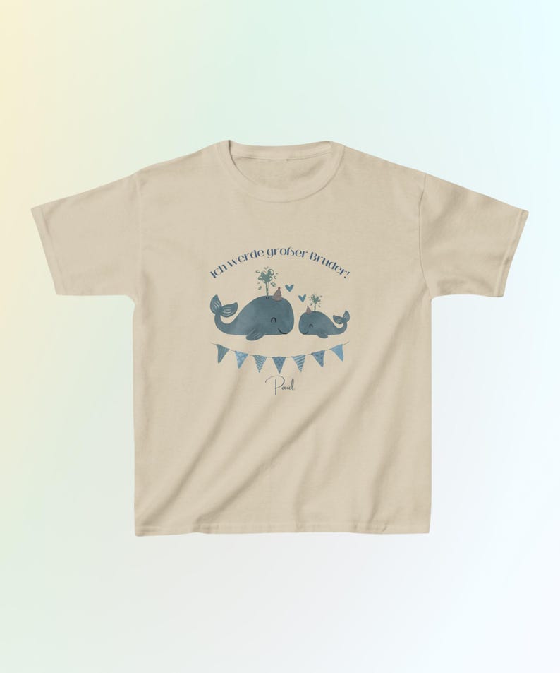 May include: A beige short-sleeve t-shirt featuring a graphic of two blue whales with party hats, a string of blue triangular bunting, and the German text Ich werde gro&szlig;er Bruder! with the name Paul printed in a dark blue script font.