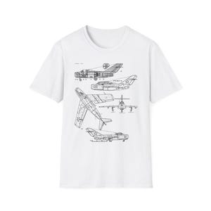May include: A white short-sleeve t-shirt featuring a black technical line drawing print of a MiG-15 fighter jet. The graphic displays multiple views of the aircraft, including side, top, and front profiles, with technical labels and markings.
