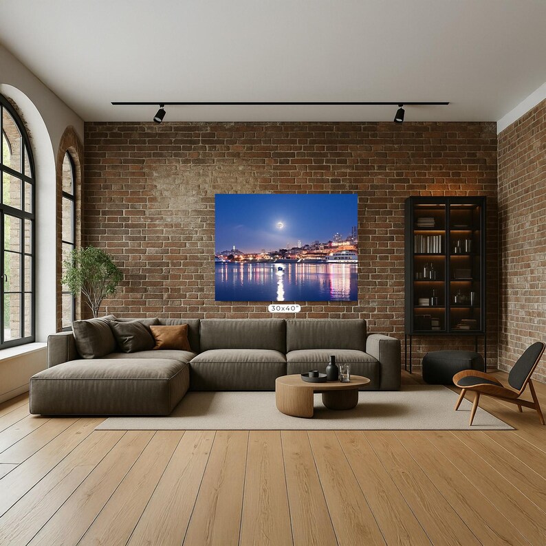 a modern living room with a large sectional sofa, a wooden coffee table, and a bookshelf. The room has a brick wall and a large window, creating a cozy and inviting atmosphere. A large painting of a city skyline is displayed on the wall, adding an artistic touch to the space.