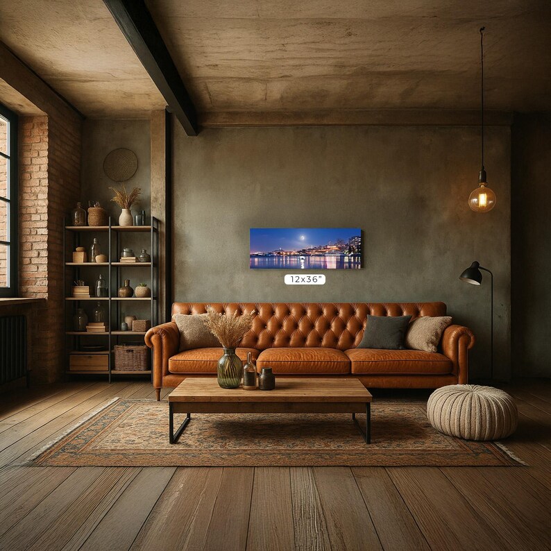 a cozy living room with a large brown leather sofa, a wooden coffee table, and a brick wall with a shelf and a painting. The room has a rustic, industrial aesthetic with exposed brick walls, a wooden floor, and a large window.