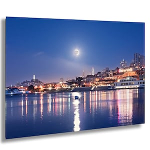 a cityscape at night, with a full moon illuminating the scene and the city's lights reflected in the water below.