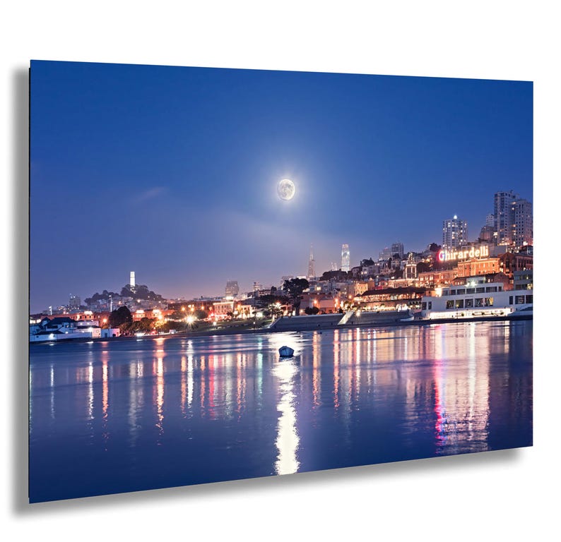 a cityscape at night, with a full moon illuminating the scene and the city's lights reflected in the water below.