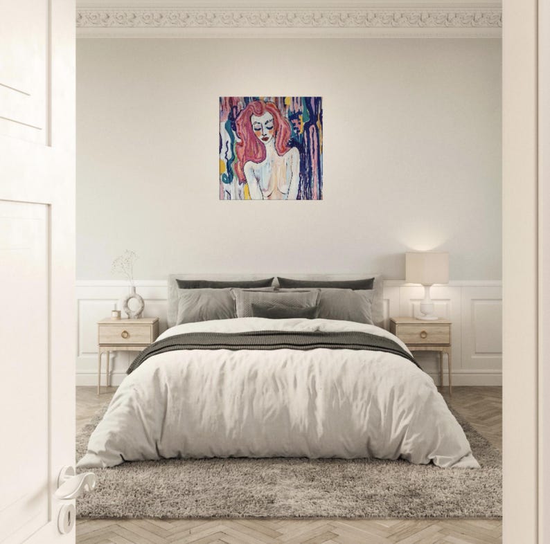 May include: An abstract painting of a woman with long pink hair and closed eyes. The artwork features a colorful background with vertical brushstrokes in shades of blue, yellow, and purple. The painting hangs above a bed with a white comforter.