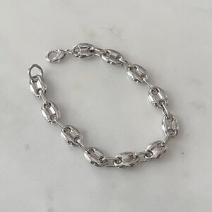 May include: A silver-colored chain bracelet with a lobster clasp. The bracelet features a series of oval-shaped links, creating a bold and modern design. The links are connected to form a flexible chain, suitable for everyday wear.