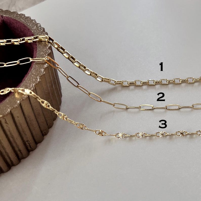 May include: Three gold-toned metal chains labeled 1, 2, and 3. Chain 1 features a square link design, chain 2 consists of elongated oval links, and chain 3 displays a delicate pattern of small, textured, star-like circular links.