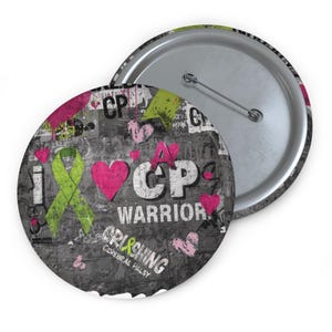 Puede incluir: Un botón redondo con un fondo gris y negro que muestra las palabras "I HEART CP WARRIOR" y "CRUSHING CEREBRAL PALSY." El diseño incluye una cinta verde, corazones rosas y las letras "CP."