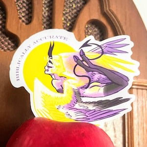 Puede incluir: Una pegatina con una ilustraci&oacute;n estilizada de una figura alada en tonos amarillos y morados. La figura est&aacute; sobre un c&iacute;rculo amarillo con el texto "Biblically Accurate". La pegatina tiene un borde blanco y una flecha negra.