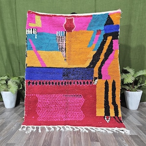May include: A rectangular area rug featuring a vibrant, multi-coloured geometric pattern with blocks of hot pink, mustard yellow, bright blue, and black. The design includes abstract shapes and a textured, shaggy pile with white fringe.