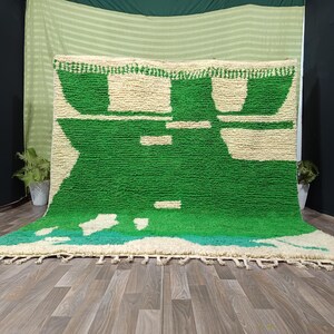 May include: A rectangular area rug featuring a high-pile, shaggy texture with a bold geometric pattern in vibrant green and off-white. The design includes large green blocks against a cream background, finished with a knotted fringe along the bottom edge.