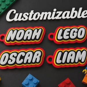 May include: Four custom keychains featuring the names NOAH, LEGO, OSCAR, and LIAM in white, bold, slanted lettering. Each keychain has a layered red, yellow, and black border with a circular hole on the left side. The word Customizable is above.