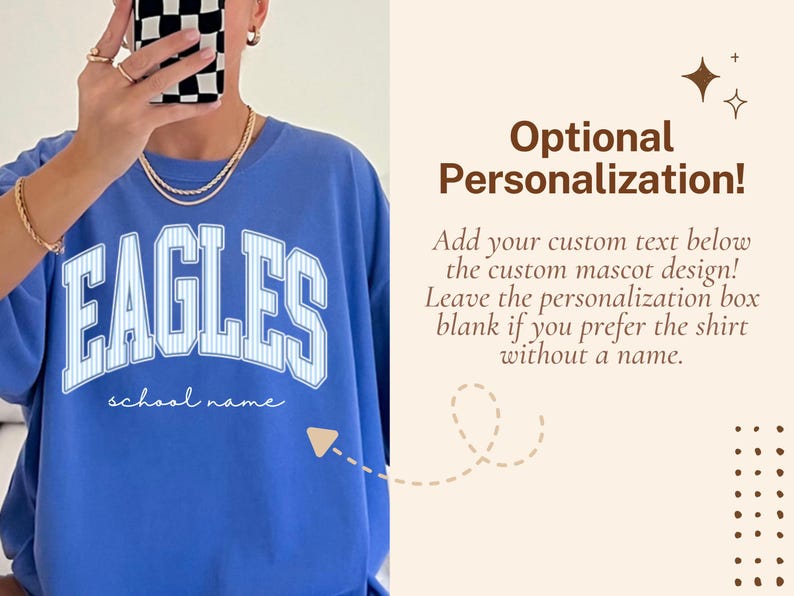 May include: A blue crewneck t-shirt featuring the word EAGLES in large white block letters with a thin blue pinstripe pattern. Below the word EAGLES, the text school name is printed in a white cursive script. The shirt has a relaxed fit.