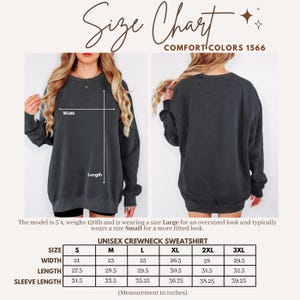 May include: A charcoal gray crewneck sweatshirt shown from the front and back with a size chart labeled Comfort Colors 1566. The chart lists width, length, and sleeve length in inches for sizes S through 3XL, with arrows indicating measurement points.