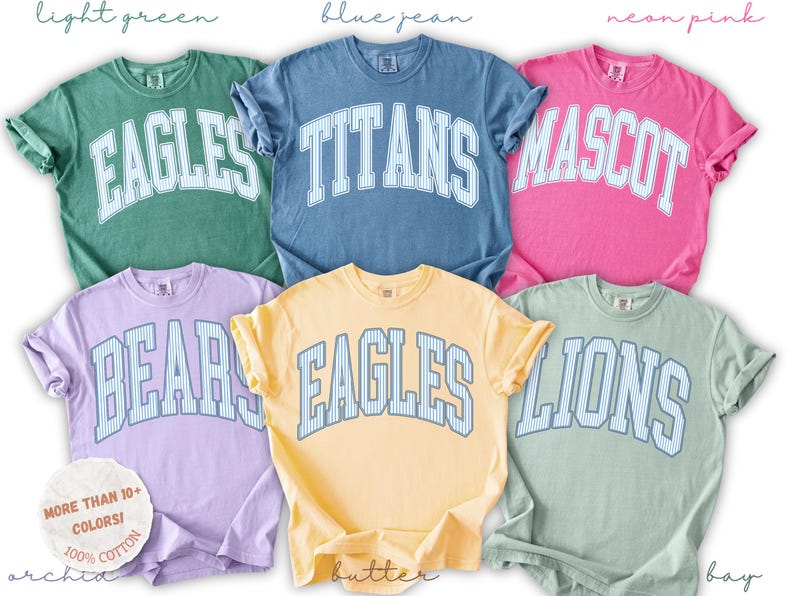 May include: Six short-sleeved crewneck t-shirts in light green, blue jean, neon pink, orchid, butter, and bay colors. Each shirt features a large arched word in white with blue pinstripes, reading EAGLES, TITANS, MASCOT, BEARS, EAGLES, or LIONS.