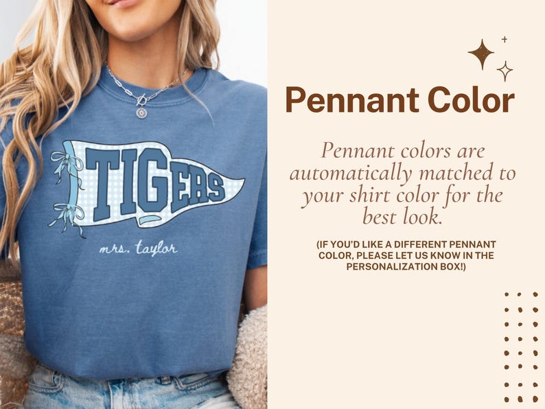 May include: A blue t-shirt featuring a white and blue checkered pennant graphic with the text TIGERS and the name mrs. taylor written below. The right side contains text about Pennant Color and personalization instructions in brown font.