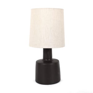 May include: A modern table lamp with a dark brown base and a beige fabric lampshade. The lamp has a cylindrical base and a tapered shade, creating a simple yet elegant design. The lamp is suitable for a bedroom or living room.