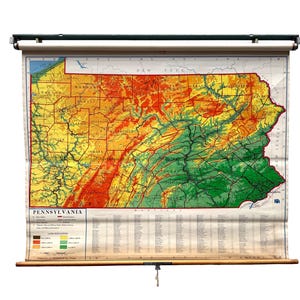 May include: A vintage pull-down wall map of Pennsylvania featuring a color-coded land elevation relief design. The map displays topographical data in shades of green, yellow, orange, and red, with a legend and text labeled Pennsylvania at the bottom.