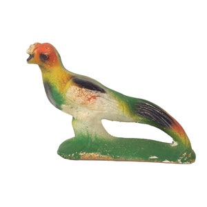 May include: A green, yellow, and orange bird figurine with a long tail. The bird is perched on a green base.