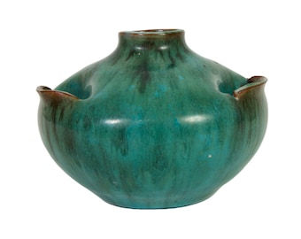 May include: A teal green ceramic vase with a rounded body and four small, rounded protrusions around the rim. The vase has a mottled glaze with brown and black accents.