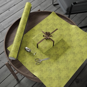May include: A roll of lime green wrapping paper with a repeating chevron pattern, a rectangular gift box wrapped in the same paper with a brown ribbon bow, a small roll of clear adhesive tape, and a pair of silver metal scissors.