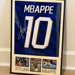 May include: Framed jersey print featuring the name "MBAPPE" above the number "10" in white. The blue jersey has an autograph and is framed with three small photos below, with the name "KYLIAN" and "MBAPPE" below the photos.
