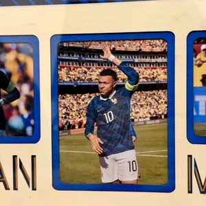 May include: A framed photograph featuring a soccer player in a blue jersey with the number 10. The player is on a green field, waving to a crowd in a stadium. The frame is cream-colored with blue accents.