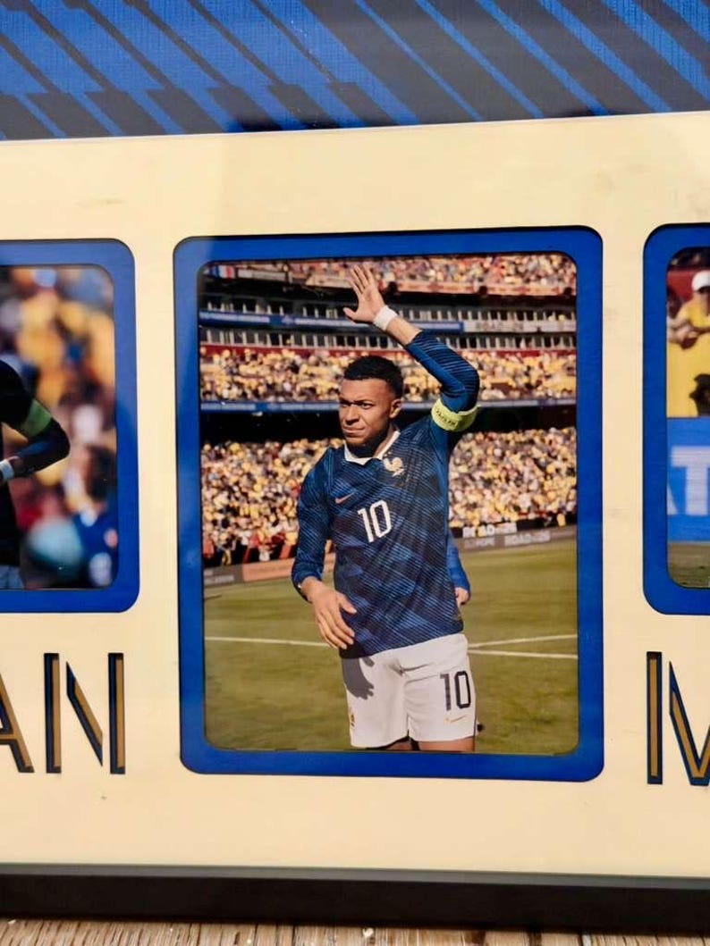 May include: A framed photograph featuring a soccer player in a blue jersey with the number 10. The player is on a green field, waving to a crowd in a stadium. The frame is cream-colored with blue accents.