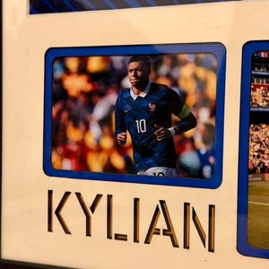 May include: Framed photo featuring a soccer player in a blue jersey with the number 10. The name "KYLIAN" is cut out in large letters below the photo. The frame has a blue border and a black frame.
