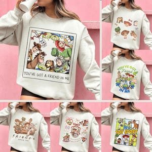 May include: A collection of light gray sweatshirts featuring various designs from the animated film "Toy Story." One sweatshirt displays a framed image of characters with the text "YOU'VE GOT A FRIEND IN ME." Other designs include character portraits and the text "TOY STORY."