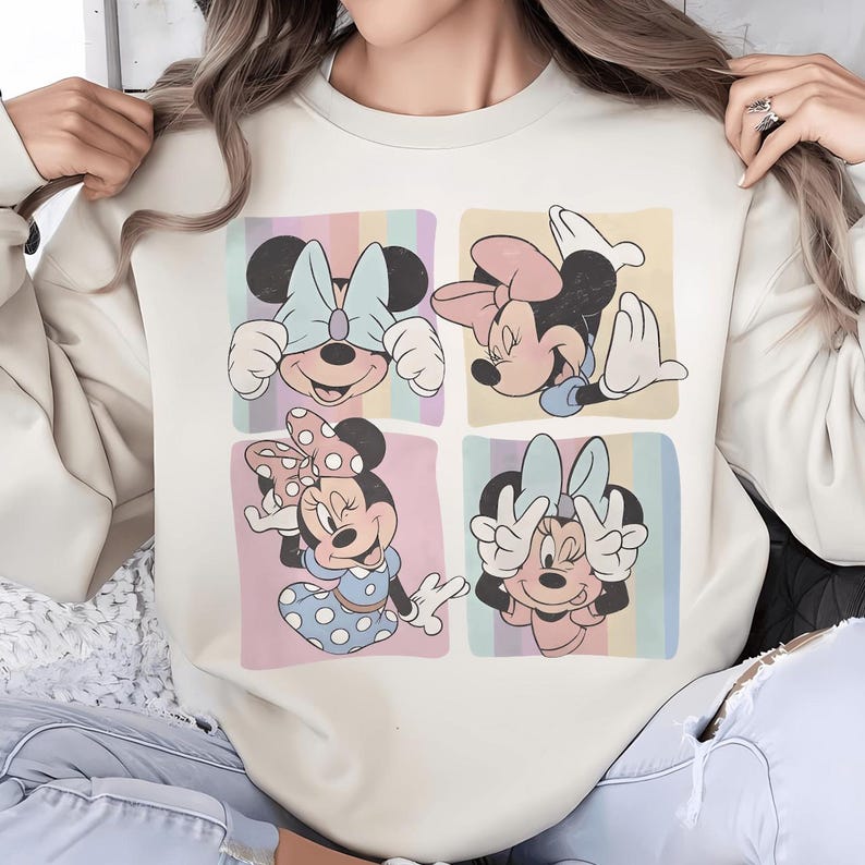 Op de afbeelding: Cr&egrave;mekleurige sweatshirt met een vierpaneels afbeelding van Minnie Mouse in verschillende poses. Elk paneel heeft een pastelkleurige regenboogachtergrond. Minnie draagt in elk paneel verschillende strikken en outfits. De sweatshirt heeft een relaxte pasvorm.