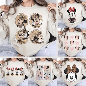 Op de afbeelding: Beige sweatshirts met verschillende Minnie Mouse-ontwerpen. E&eacute;n sweatshirt toont vier Minnie Mouse-illustraties met luipaardprint accenten. Andere ontwerpen zijn onder meer Minnie Mouse met strikken, Minnie Mouse in verschillende poses en een close-up van Minnie Mouse's gezicht met een luipaardprint strik.