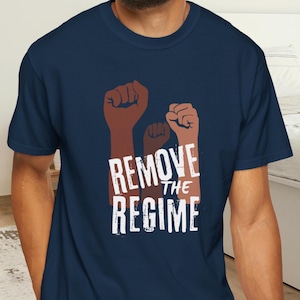 May include: Navy blue t-shirt featuring three raised fists in shades of brown and the text "REMOVE THE REGIME" in white. The shirt is made of a soft material.