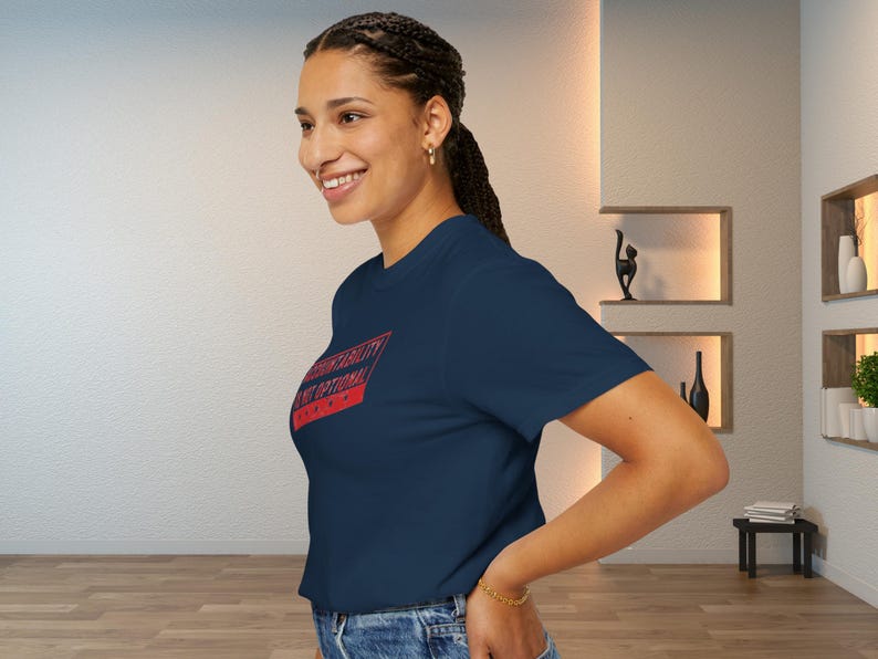 May include: Navy blue t-shirt with the text "Authenticity is Optional" in a red and white rectangular design. The model is wearing blue jeans and a gold bracelet.