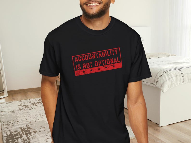 May include: Black crew neck t-shirt featuring the red text "ACCOUNTABILITY IS NOT OPTIONAL" in a rectangular stamp design. The shirt is made of a soft material and is suitable for casual wear.