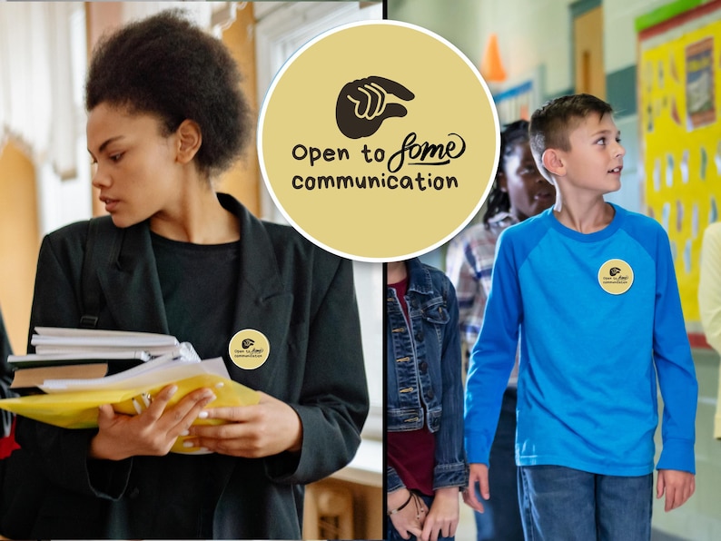 May include: A round, tan button with the words "Open to some communication" and a hand symbol. The button is worn on a black blazer and a blue long-sleeve shirt. The image shows people in a school setting.