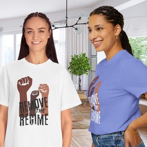 May include: Two people wearing t-shirts with a graphic of three raised fists in shades of brown. The text "REMOVE THE REGIME" is printed below the fists. One shirt is white, the other is light blue.