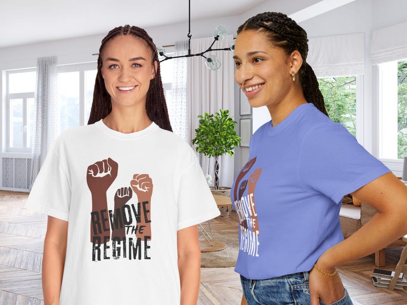 May include: Two people wearing t-shirts with a graphic of three raised fists in shades of brown. The text "REMOVE THE REGIME" is printed below the fists. One shirt is white, the other is light blue.