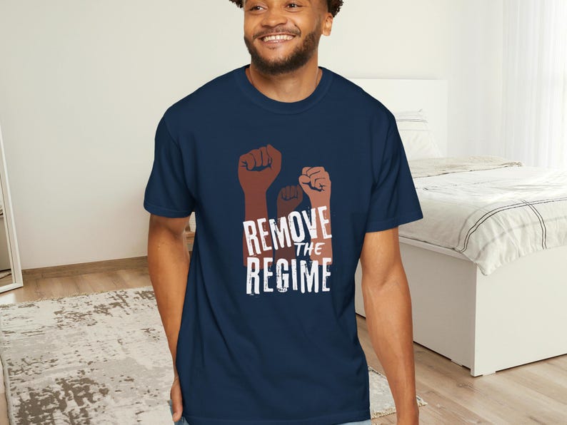 May include: Navy blue t-shirt featuring three raised fists in shades of brown and the text "REMOVE THE REGIME" in white. The shirt is made of a soft material.