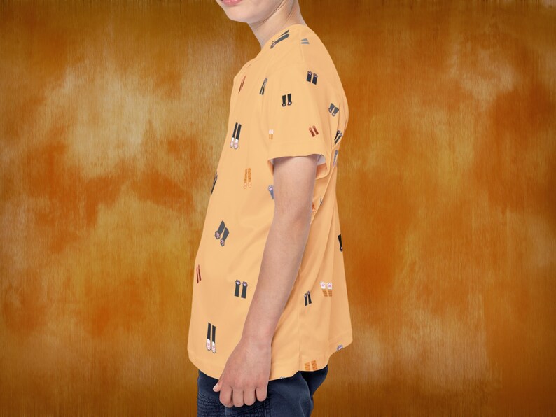 May include: A short-sleeved, peach-colored t-shirt with a repeating pattern of black and white shoe illustrations. The shirt is worn by a person and paired with dark blue pants. The background is a textured orange.