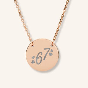 May include: Rose gold necklace with a circular pendant. The pendant displays the number "67" in a stylized font, with heart symbols. The necklace chain is also rose gold.