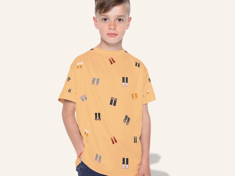 May include: Mustard yellow t-shirt with a repeating pattern of colorful shoe illustrations. The short-sleeved shirt is worn by a young person. The shoes are in various colors, including red, blue, and black.
