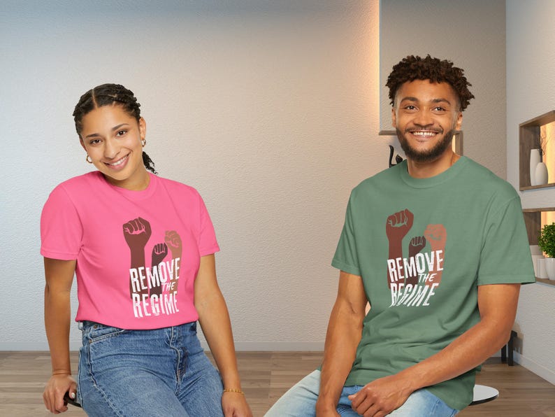 May include: Two people wearing t-shirts with the text "REMOVE THE REGIME" and a graphic of three fists. One shirt is pink, the other is green. Both shirts have short sleeves and are made of a soft material.