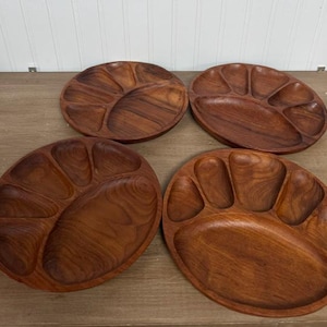Könnte beinhalten: Vier runde Servierplatten aus Holz mit einer reichen braunen Maserung. Jede Platte verfügt über ein großes, zentrales, oval geformtes Fach, das von fünf kleineren, separaten Abschnitten umgeben ist, die halbkreisförmig am Rand angeordnet sind.
